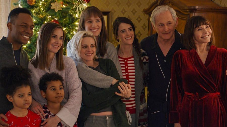 A still from Happiest Season of several people smiling in front of a Christmas tree. 