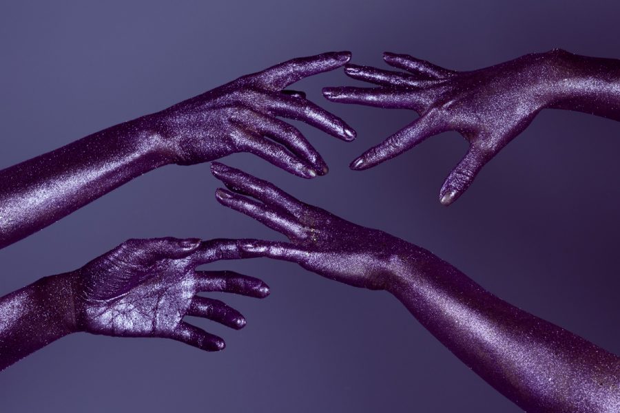A pair of hands painted in purple glitter, reaching out to each other and representing community, connection and coming out.