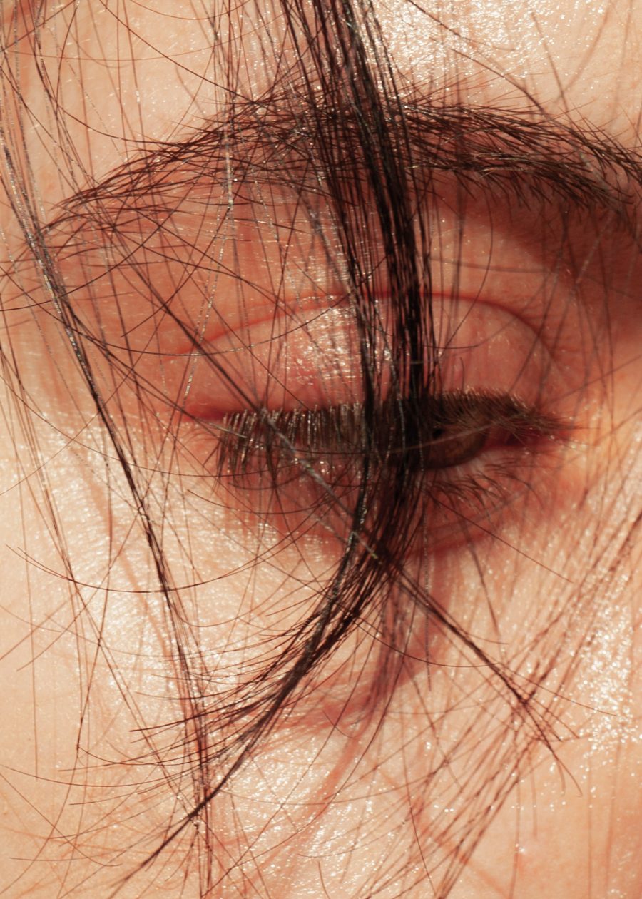 A close-up of a person's eye, with a strand of dark hair falling over their face.