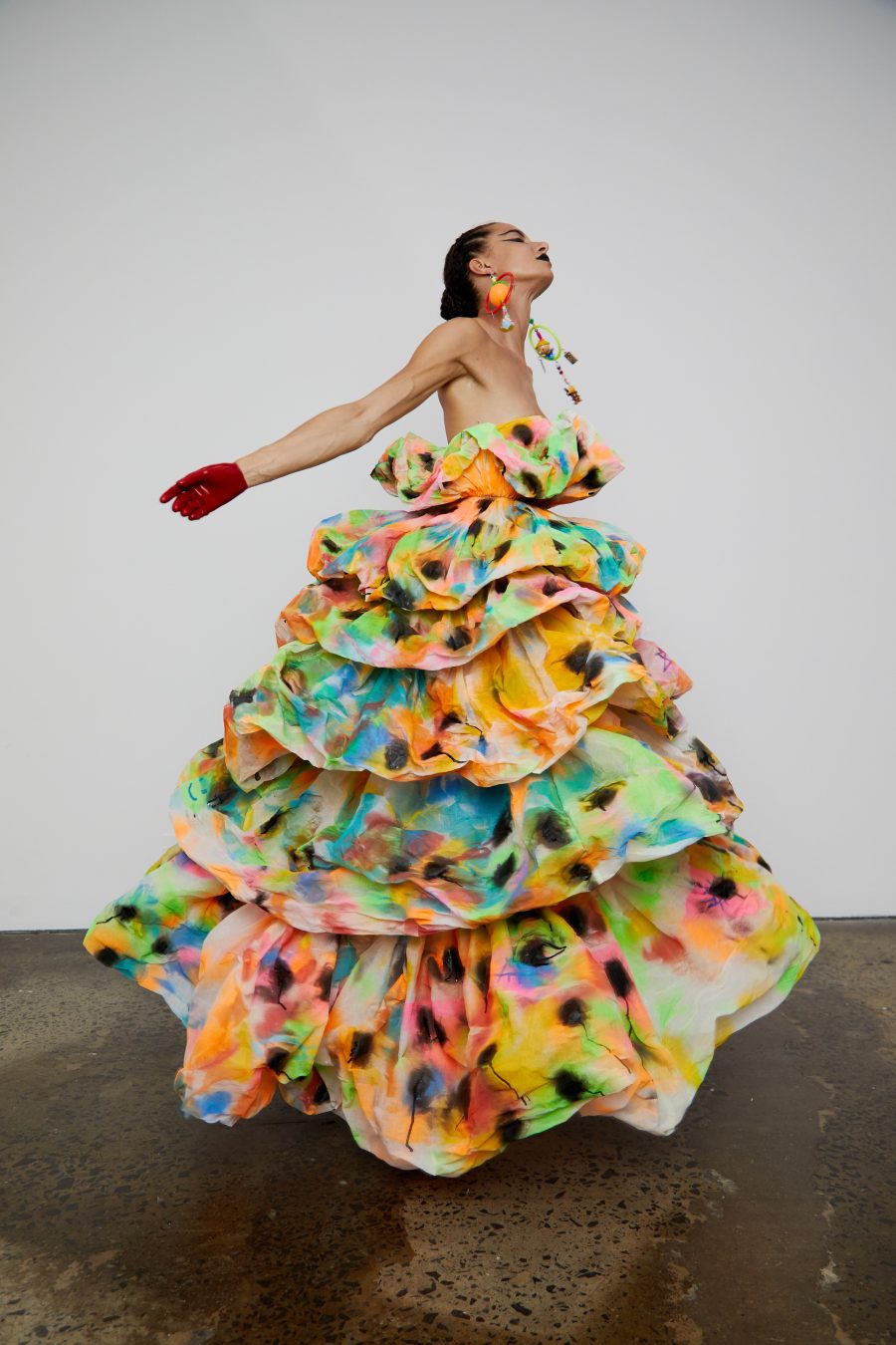 A person wearing a frilly spray-painted gown with their arms outstretched.