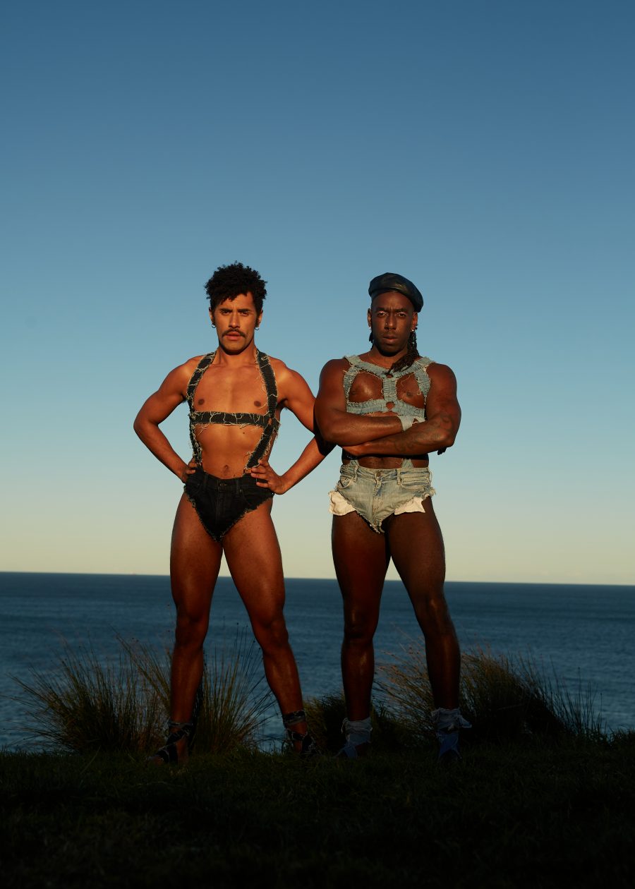 Two people in front of the ocean wearing denim harnesses and hot pants. Taken by Lexi Laphor.