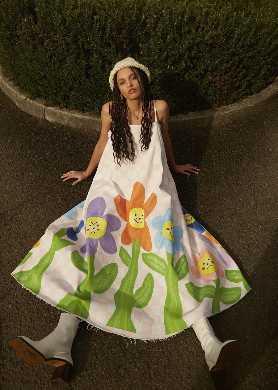 A person sitting on the ground in a dress with painted flowers on it.