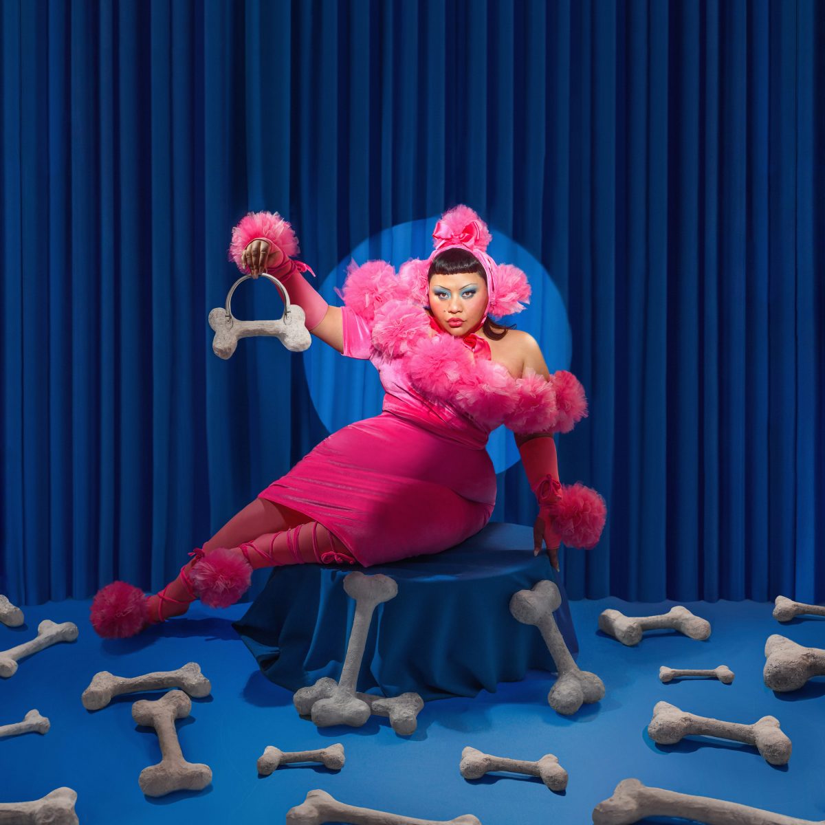 Kira Puru in a poodle-inspired pink outfit surrounded by prop bones.