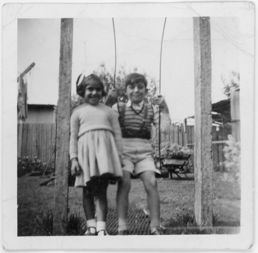 Archival photo of two young siblings on a playground swing.