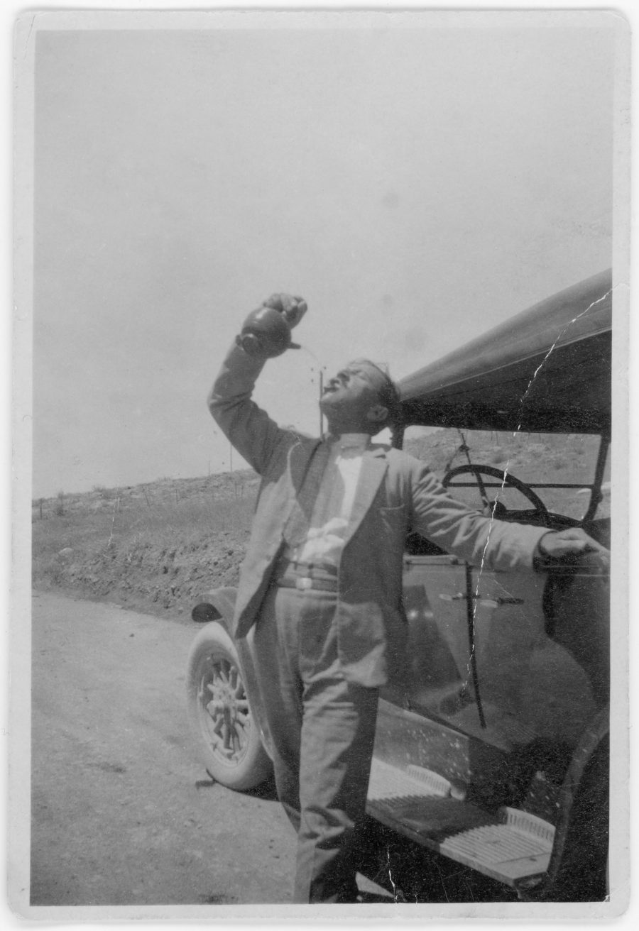 Archival photo of Abdullah Sahhar pouring water into his mouth from an ibrik, standing in front of a car.