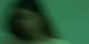 Blurred image of a person in a dimly lit room.