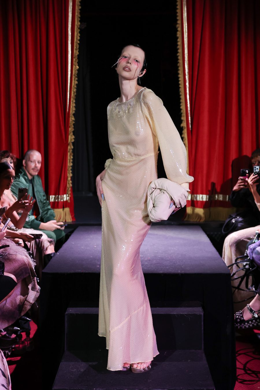 A model wearing a pale pink gown and holding a hand-shaped handbag.